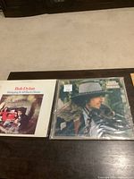 Two Bob Dylan LP records side by side on a table, both in their original sleeves with plastic covers on one album.