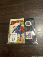 Front view of sealed pack showing Superman comic style cover with visible lenticular coin and stamp inside.