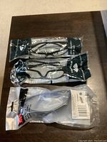 Three safety glasses in original packaging, two Pyramex and one 3M, displayed on a dark wood surface.