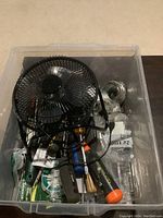 View of plastic storage container filled with assorted construction hand tools and supplies including hammers, screwdrivers, wrench, electrical tape, and other small hardware items.