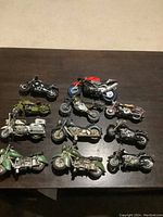 Overview of 11 toy motorcycles varying in colors, styles, and conditions spread on dark surface