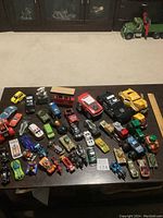 Wide shot of the full assortment of toy vehicles including many miniature cars lined up on a dark surface.