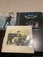 Three Neil Young LP record albums in their original sleeves displayed on a dark surface: 'Comes A Time,' 'Everybody Knows This Is Nowhere,' and 'Rust Never Sleeps'.