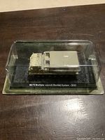 Front view of sealed Amercom die cast M270 Multiple Launch Rocket System model in clear plastic display case with cardboard backing.