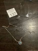 Full view of silver chain necklace with heart-shaped pendant on wooden surface.