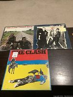 Three The Clash LP albums displayed on a wooden surface, showing album cover artwork including 'Combat Rock' and two others with band images.