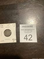 Coin and holder with auction lot number 42 beside it on table surface.