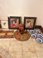Overview of entire lot on tiled floor showing framed art, textile, tray, mask, small items and plates