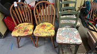 View of all four chairs showing two natural wood Jamco chairs with yellow floral cushions and two green painted AIG ladder back chairs with floral cushions.