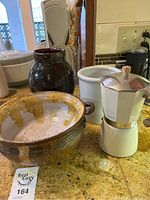 Coffee maker, ceramic bowl, white ceramic container, and dark brown pottery vase on kitchen counter
