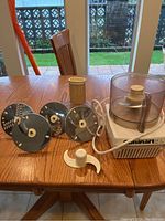 Food processor unit on wooden table with 5 metal blades and plastic blade holder displayed