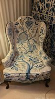 Full front view of the embroidered wingback armchair showing overall shape, upholstery pattern, seat cushion, and cabriole legs