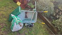 Overview of the lot showing the metal wheelbarrow, pot dolly, peat moss bag, and planter tray on grass near a garden bed.