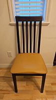 Front view of one dining chair with wooden black frame and yellow cushioned seat.