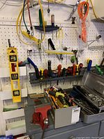 Wide view of pegboard with spirit level, clamps, screwdrivers, and metal toolbox on workbench beneath.