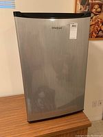 Front view of stainless steel Whirlpool bar fridge on wood surface.