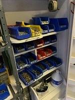 Shelves with blue, red, and yellow plastic bins containing assorted bolts, screws, and fasteners organized by size.