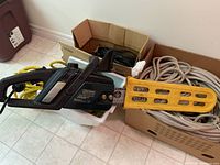 Electric chain saw laying on the floor alongside boxes of ropes, showing the Craftsman branding and yellow bar cover.