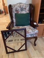 Upholstered cane armchair with floral upholstery and green pillow, wooden framed mirror leaning against the chair.