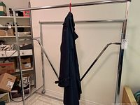 Full view of metal clothing rack with a dark coat hanging on a red hanger, showing its size and structure.
