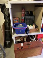 Photo of shelving unit with boxed plastic liners, plastic bottles, blue laundry basket, and storage organizer drawers with small compartments.