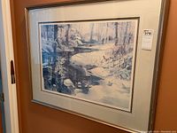 Framed winter scene artwork by Brent Heighton titled 'Reflections of Winter', showing a snow-covered river and trees in muted blues and grays, hanging on a wall.