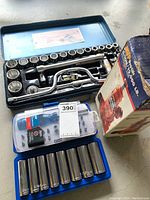 Overview of hydraulic jack boxed and various socket tools and bit sets arranged on floor.