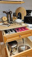 Overview of kitchen countertop and two open drawers showing knives in block, small appliances, utensils, and cookware inside drawers