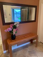 Large rectangular wooden framed mirror hanging on a wall above an oak sofa table, showing part of the hallway and the front door reflected in the mirror.