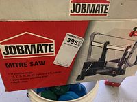 Red and white JOBMATE box for mitre saw showing brand and product details including 11 positive stops, mitre angles, quick-release lever, and depth stops.