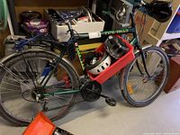 Side view of green Pine Hill bicycle with attached bike carrier, red plastic bin holding a white and black helmet, and pump on floor