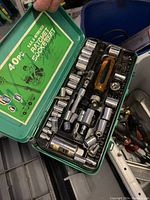 Opened green case displaying organized chrome sockets, socket wrenches, and screwdrivers.