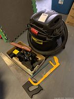Photo showing the 4 gallon black shop vacuum with hose, box with vacuum attachments, and yellow-handled hand saw.