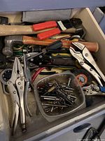 Drawer with assorted hand tools such as pliers, hammers, drill bits in a container and clip clamps with red handles