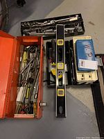 Overview of the tools lot showing the orange metal toolbox, black socket set case, spirit level, and small plastic toolbox.
