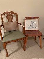 Side view of the two vintage chairs: armchair with cane back and green cushion on left, simpler wooden chair on right with framed artwork resting on it.