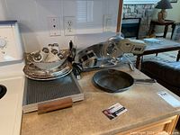 Warming tray, meat slicer, cast iron frying pan arranged on kitchen counter.