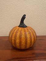 Front view of the silica crackle glazed decorative pumpkin with a black stem on a wooden surface.