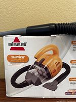 Photo of the original box showing Bissell Cleanview Deluxe hand vacuum in yellow and gray with hose and wand attachments
