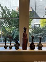 Full view of six items including five vases and a statue on window sill with outdoor greenery background.