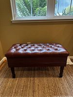 Front view of tufted brown leather piano stool with wooden legs.