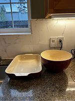 Photo of red ceramic rectangular baking dish with cream interior next to a large red ceramic mixing bowl on a granite countertop