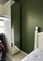 Full view of the tall cabinet showing the mirrored front door and white sides against a green wall.