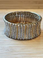 Thick bangle bracelet with rows of clear rhinestones on gold-tone metal base shown from a side angle.