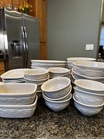 Multiple stacked bowls in round and rectangular shapes with basket-weave texture, white vitrified pottery material.