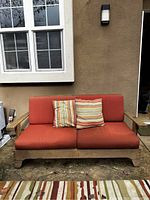 Front view of wooden bench with cushions and throw pillows in exterior setting