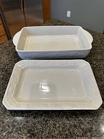 Top view of the two Longaberger vitrified pottery baking pieces in cream color on countertop. Shows the deeper pan and shallower sheet with embossed basketweave pattern on sides.