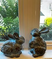 Porcelain rabbit figurines positioned side by side on a window ledge showing textured fur detail and ear positioning