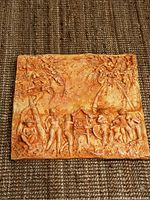 Full view of the rectangular wood carving showing village scene with figures and trees.