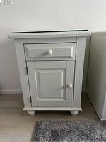 Front view of the white Pottery Barn nightstand showing the drawer, cabinet door, and glass top